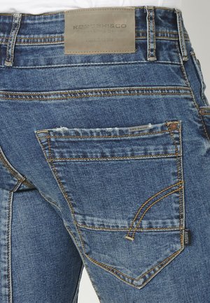 Farkut keskipitkässä sinisessä, tekstuurilla varustettuna. Vyötäröllä on nahkainen etiketti ja taskuissa on erottuva tikkaus.