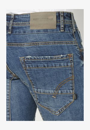 Keskmise sinise värvusega teksad, millel on tekstuuriga viimistlus. Vöövahel on nahklabel ja taskute ääres kontrastne õmblus.