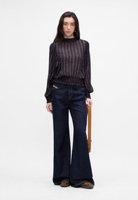 Blusa a righe navy con maniche a svaso e vita arricciata; jeans flared in denim scuro a vita alta; ballerine con stampa animalier; borsa a tracolla marrone.