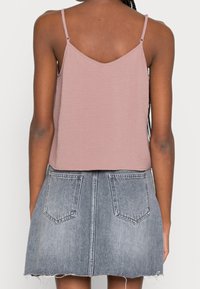 Haut sans manches couleur rose poussiéreux avec fines bretelles, associé à une jupe en jean délavé clair avec deux poches arrière et un ourlet effiloché.