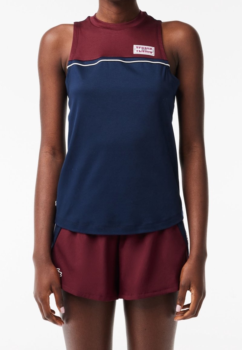 Marinblå ärmlös sporttopp med vinröda detaljer och en logotyp, kombinerad med vinröda shorts med sidofickor och avslappnad passform.