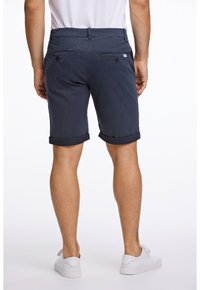 Marinblå shorts med rullade fållar, tillverkade av mjukt tyg. Har två bakfickor med knappar. Enkel, skräddarsydd design.