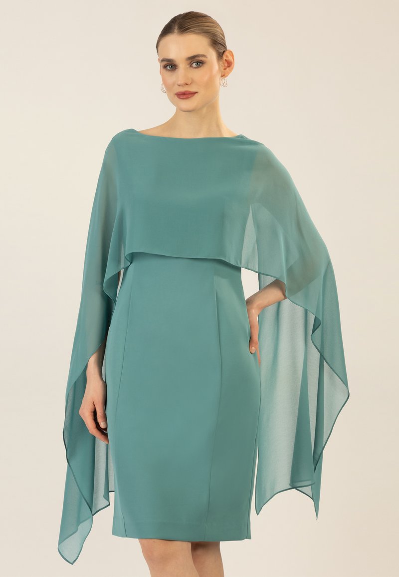 Elegantes türkisfarbenes Kleid mit einem fließenden, transparenten Überwurf. Glatte Textur, taillierte Silhouette und ein eleganter Bootsausschnitt.