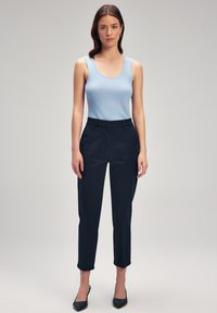 Top a canottiera azzurra a coste abbinato a pantaloni sartoriali blu scuro. I pantaloni presentano una vestibilità dritta e una leggera lunghezza alla caviglia. Tacchi neri a punta.