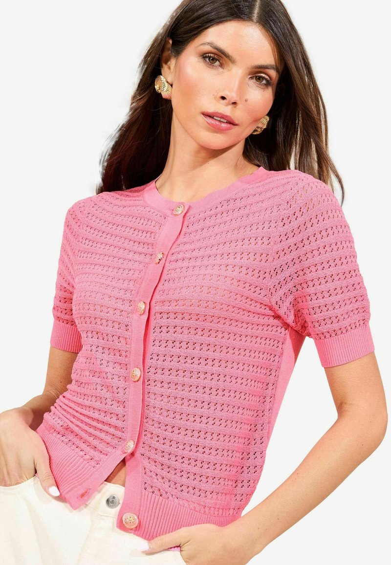 Rosa stickad cardigan med korta ärmar, med ett strukturerat mönster och knappstängning. Ribbad kant ger extra designdetalj.