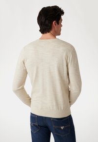 Hellbeige gestrickter Pullover mit langen Ärmeln, Rundhalsausschnitt und geripptem Saum, getragen über dunklen Jeans, zeigt einen strukturierten, weichen Stoff.