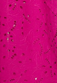 Tessuto fucsia con ritagli floreali, caratterizzato da dettagli cuciti e perforazioni circolari. La texture appare leggera e ariosa.