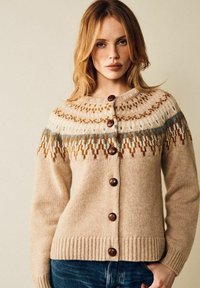 Beige stickad cardigan med rund halsringning, med en mönstrad okdel i brunt och blått, och träknappar fram. Ribbad nederkant.