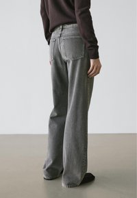 Grijze denim jeans met wijde pijpen en gewassen textuur, voorzien van twee achterzakken en een hoge taille, gestyled met een bruine trui.