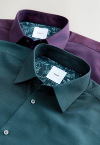 Dwie koszule z kołnierzykiem; jedna w głębokim fioletowym, druga w ciemnym zielonym. Obie mają kwieciste wzory wewnętrznych podszewek i zapięcia na guziki.