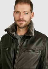 Chaqueta de cuero negra con un suave cuello forrado de piel gris, que presenta bolsillos con cremallera, cierre frontal con cremallera y una textura suave.