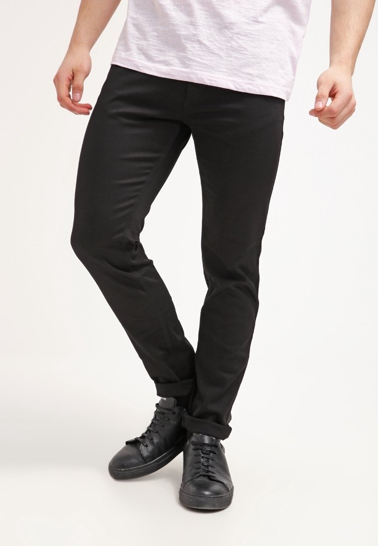 Pantalon noir ajusté en coton à texture lisse. Ourlets retroussés et associé à des baskets noires à lacets.