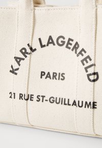 Beżowa torba płócienna z czarnym napisem "KARL LAGERFELD PARIS 21 RUE ST-GUILLAUME" i dwiema wszytymi rączkami.