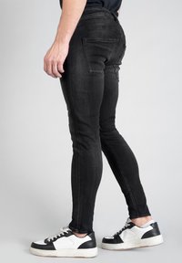Jean slim noir en denim, avec un design à cinq poches et des détails de décoloration. Associés à des baskets noir et blanc.