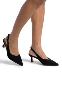 Escarpins noir en daim avec un bout pointu, un talon fin et une bride réglable ornée d'un bouton décoratif. Doublure intérieure lisse.