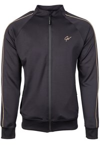 Zwarte ritsjack gemaakt van gladde stof, met gouden accenten langs de schouders en zijzakken met ritssluitingen.