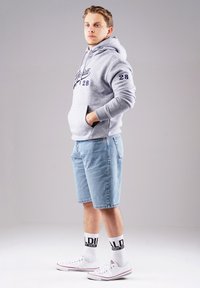 Grauer Hoodie mit blauer Schrift, hellblaue Denim-Shorts, weiße Socken mit schwarzen Akzenten und weiße Sneakers. Lässiges Outfit-Design.