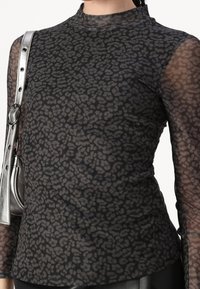 Top nero trasparente a maniche lunghe con un motivo animalier grigio, caratterizzato da un design a collo alto e una trama liscia. Completato da accessori in argento.