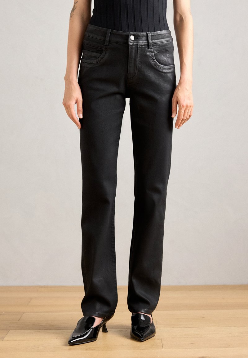 Svarta jeans i denim med slim fit, två framfickor med rundade kanter och medelhög midja, kombinerat med svarta spetsiga klackar.