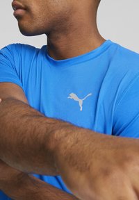 Modrá sportovní tričko s krátkými rukávy, kulatým výstřihem a reflexním logem Puma na prsou. Hladká, lehká tkanina.