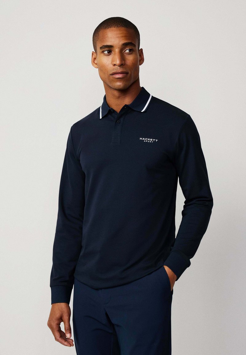 Polo de manga larga en color navy con un cuello blanco ribeteado, tapeta de botones en la parte frontal y detalles del logo en el pecho; fabricado con un tejido suave y liso.