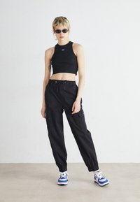 Black cropped tank top with a blue logo, paired with black cargo pants featuring drawstring, elastic cuffs, and pockets. Blue and white sneakers.