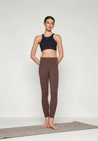 Fekete sportmelltartó és barna leggings, rugalmas anyagból készült. A leggings testhez simuló, a bokáig ér. Egyszerű dizájn, nincsenek látható minták vagy fémszárak.