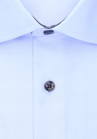 Tissu de chemise bleu clair avec une texture diagonale, comprenant un bouton noir au col et des détails de couture subtils.