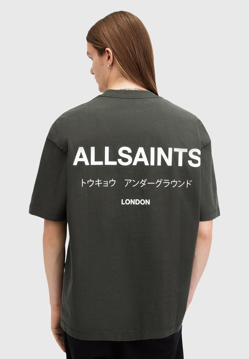 Camiseta de algodón verde oscuro con mangas cortas y cuello redondo. Presenta un gran texto blanco en la parte posterior: "ALLSAINTS" y "LONDRES".