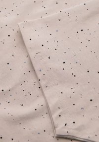 Lichtbeige stof met verspreide zwarte en lichtblauwe spikkels, met een gladde textuur en nette stiksels langs de randen.