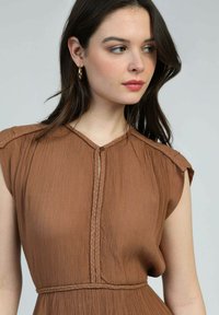 Robe plissée marron avec un décolleté en V, un bord tressé et une fermeture à boutons. Manches courtes et tissu doux et texturé.