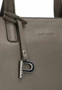 Borsa a mano in pelle grigia con una texture liscia, caratterizzata da un charm argento a forma di "P" e il nome del marchio "PICARD" impresso sul lato.