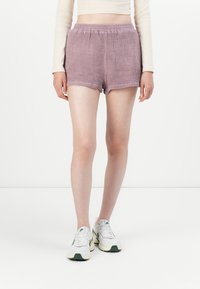 Shorts à carreaux violets avec une taille �élastique, offrant une coupe ample et une texture lisse. Portés avec des baskets de couleur claire.