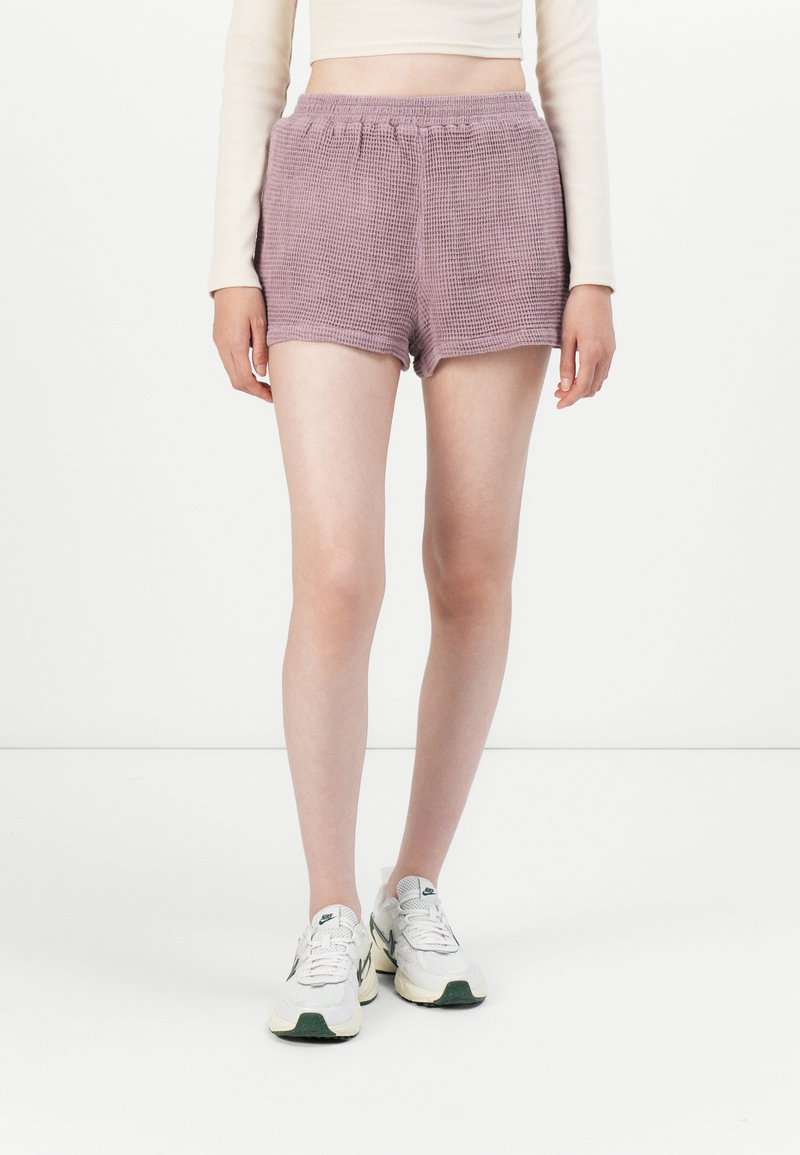 Shorts à carreaux violets avec une taille élastique, offrant une coupe ample et une texture lisse. Portés avec des baskets de couleur claire.
