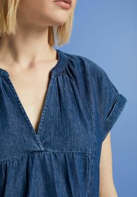Denim blouse with a V-neck, gathered detailing at the shoulders, short sleeves, and a loose fit. Color is deep blue with a soft texture.