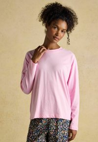 Light pink long-sleeve shirt made of soft fabric; crew neckline and relaxed fit. Paired with floral-patterned pants.