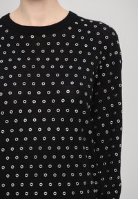 Maglione nero a maglia con scollatura tonda e occhielli bianchi sparsi per texture. Maniche lunghe con forma aderente.