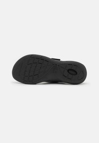 Suola di scarpa in gomma nera con un motivo testurizzato, scanalature stampate e un dettaglio del logo in rilievo. Progettata per offrire trazione e comfort.