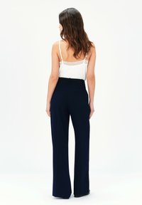 Königsblaue, hoch taillierte Hosen mit geradem Bein und zwei Gesäßtaschen. Das Outfit wird mit einem weißen, spitzenbesetzten Trägertop kombiniert.