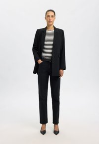 Svart blazer over en svart og hvit stripet skjorte, parret med svarte jeans og spisse svarte hæler. Enkelt, skreddersydd design og silhuett.