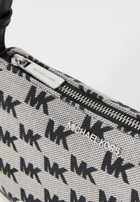 Black and gray patterned handbag featuring a repeating "MK" logo, a textured fabric, and a silver zipper with a branded pull tab.
