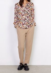 Blusa floreale con maniche lunghe, sfondo nero, fiori arancioni, rosa e crema. Abbinata a pantaloni beige e mocassini neri chunky.
