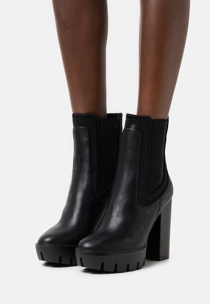 Bottines en cuir noir avec panneaux latéraux élastiques, talon haut carré et semelle épaisse texturée. Finition lisse avec détails de coutures contrastées.
