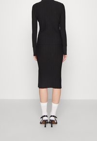 Svart ribbad stickad långärmad topp kombinerad med en matchande pennkjol. Strumpor och remklackar fullbordar outfiten.