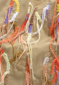 Haftowana tkanina z fakturowanymi, wielokolorowymi nićmi w odcieniach czerwieni, brązu, żółci i fioletu na beżowym tle, z luźno wystającymi nitkami.