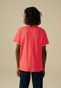 Polo a maniche corte di colore rosa brillante con superficie testurizzata, rifiniture bianche sul colletto e sulle maniche, e un fit rilassato.