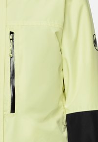 Gelbe wasserdichte Jacke mit schwarzen Akzenten, ausgestattet mit einer Reißverschlusstasche auf der Brust, glatter Textur und verstellbarem Zugband am Kragen.
