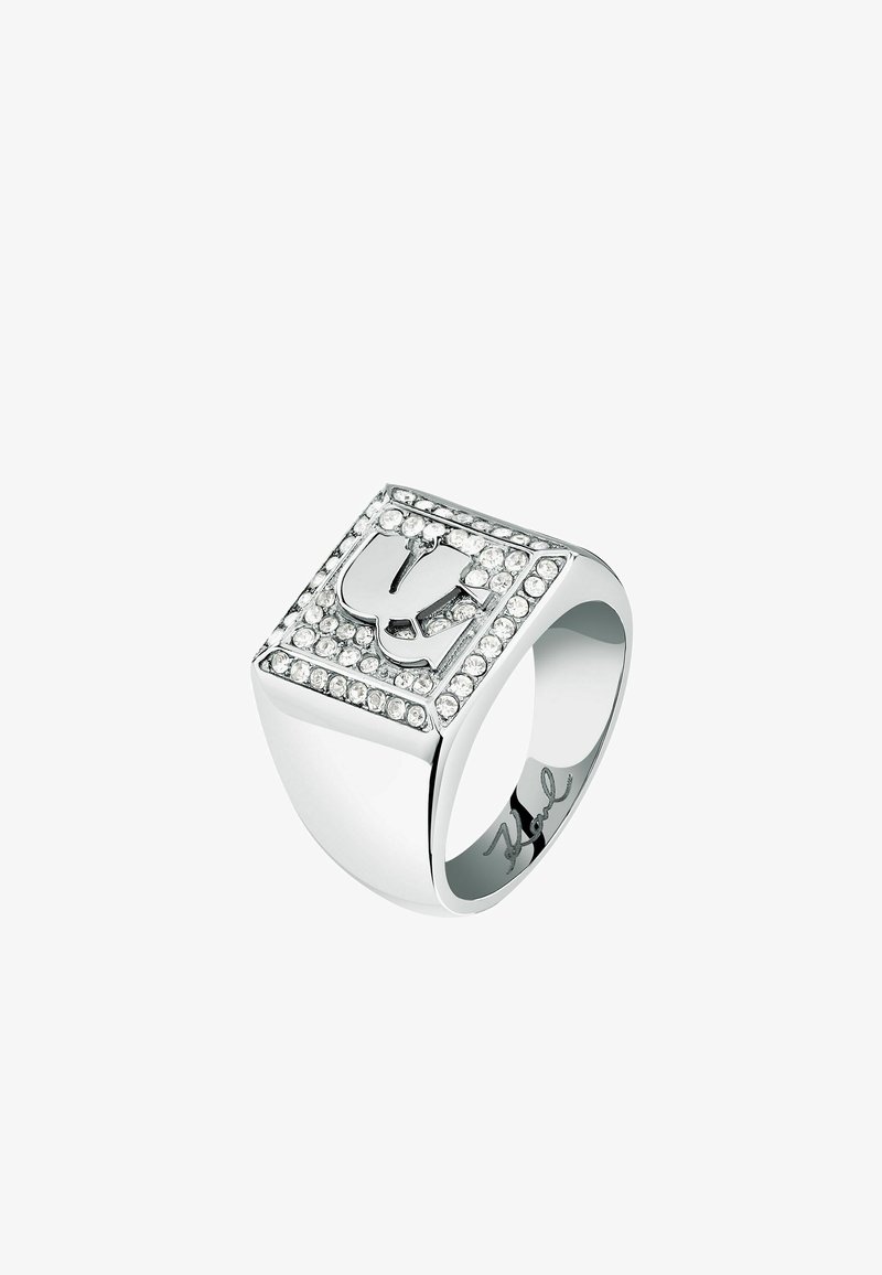 Silberfarbener Ring mit quadratischer Fassung, featuring ein erhabenes Design und umgeben von Strasssteinen. Glatte, glänzende Oberfläche; eingravierte Signatur im Inneren.