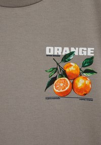 Tres naranjas con hojas verdes, una cortada en rodajas, debajo del texto en negrita blanco "NARANJA" sobre un fondo de tela gris.