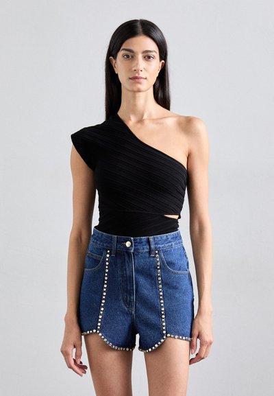 Schwarzes Top mit einem Schulterriemen aus strukturiertem Stoff, kombiniert mit hoch taillierten blauen Jeansshorts mit Nietenakzenten entlang der Nähte.